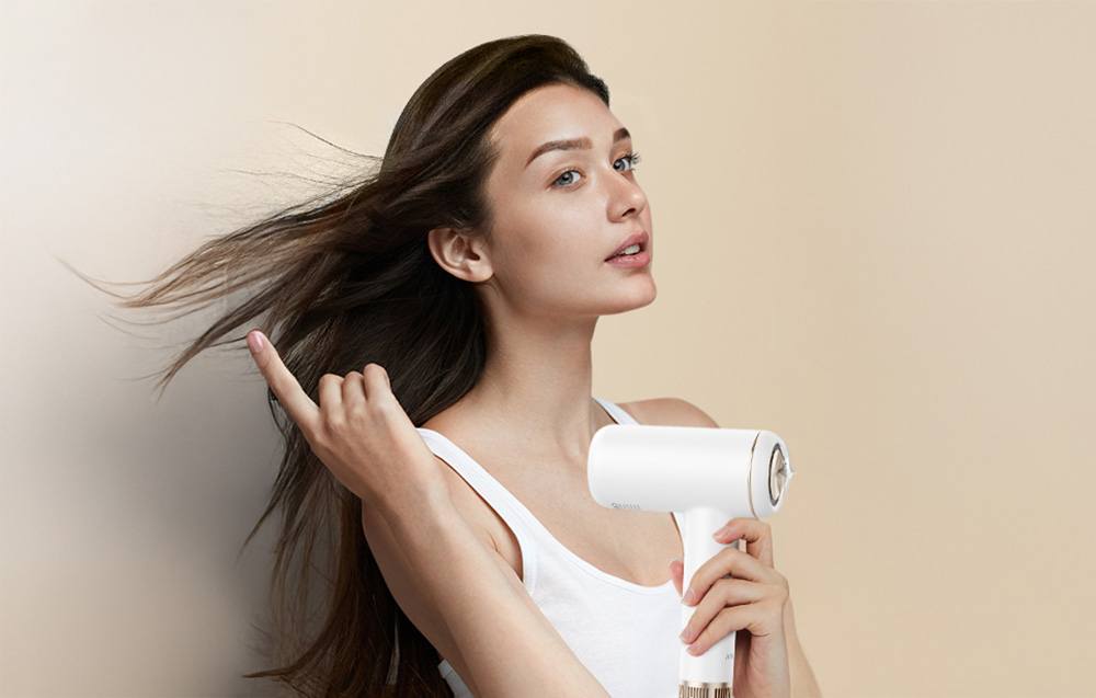 Femme en haut blanc séchant ses cheveux avec un sèche-cheveux blanc
