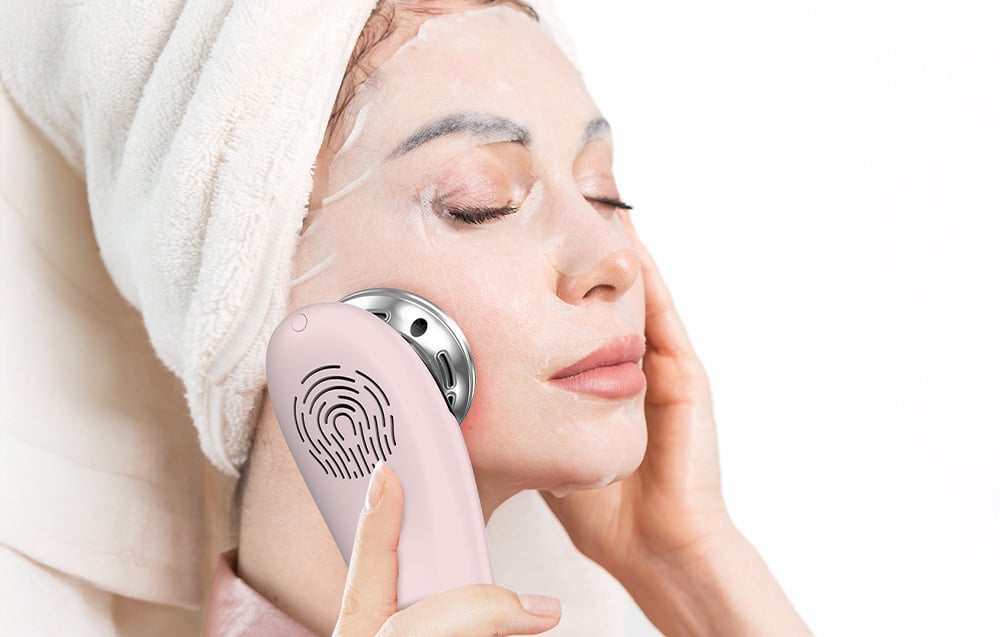 Femme avec un masque facial utilise un masseur facial