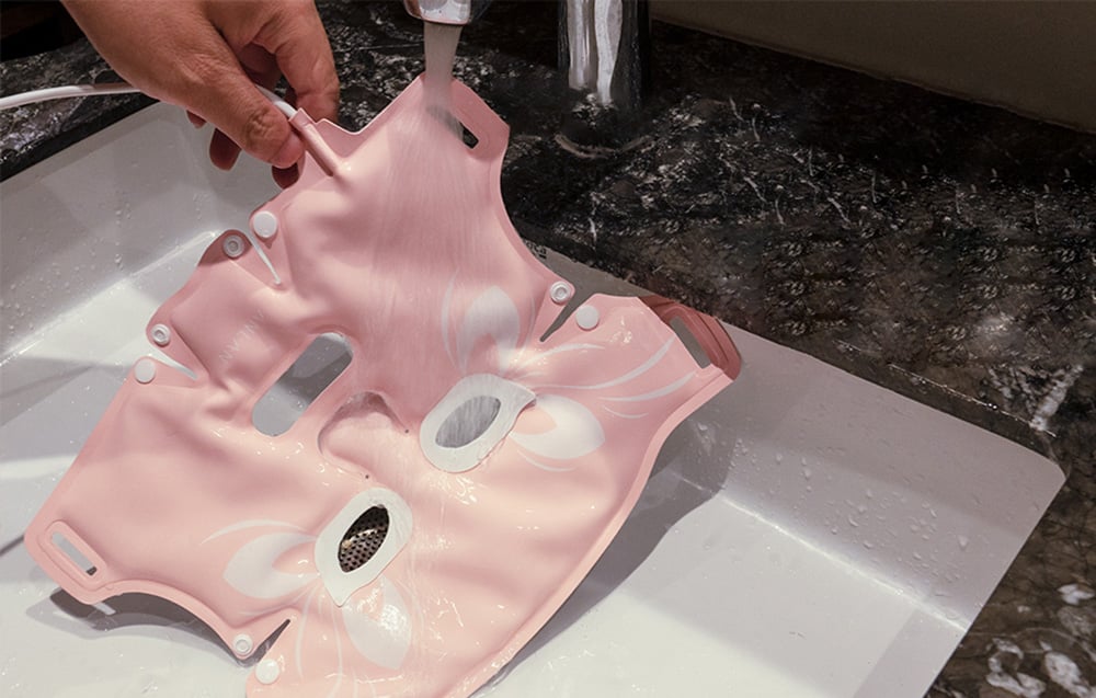 Mains lavant un masque en silicone rose sous l'eau courante dans un évier