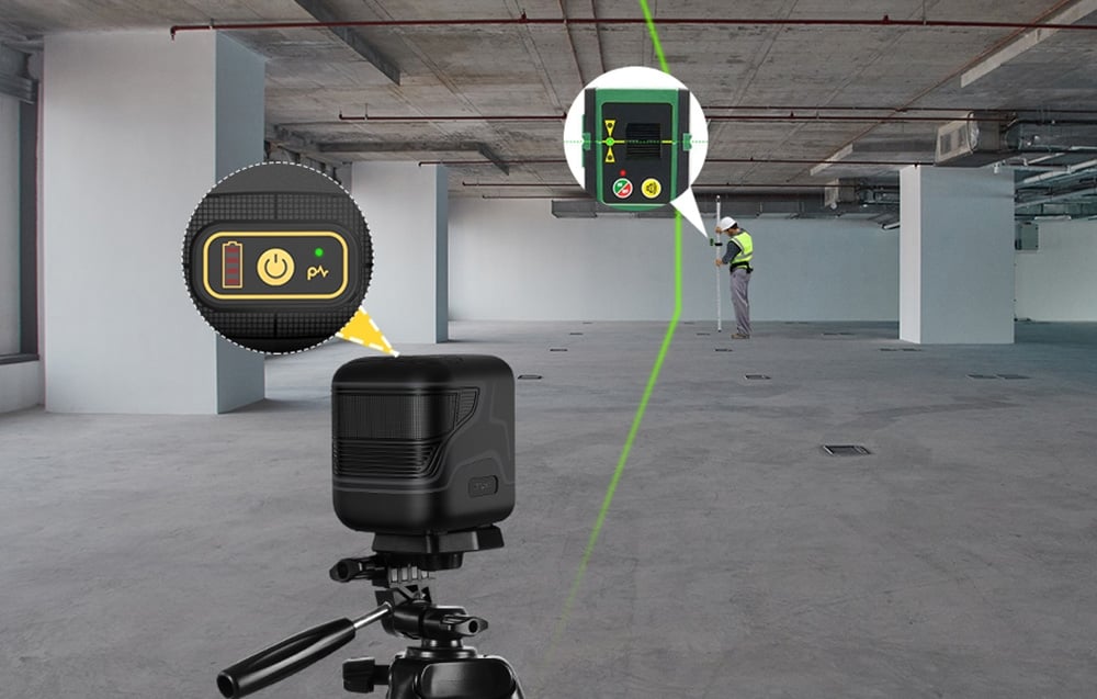 Un niveau laser placé dans un garage souterrain. Au loin, un homme portant un casque et un gilet réfléchissant.