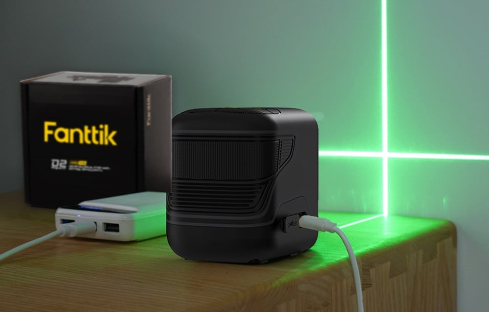 Le niveau laser Fanttik repose sur une table en bois connecté à une batterie externe blanche.