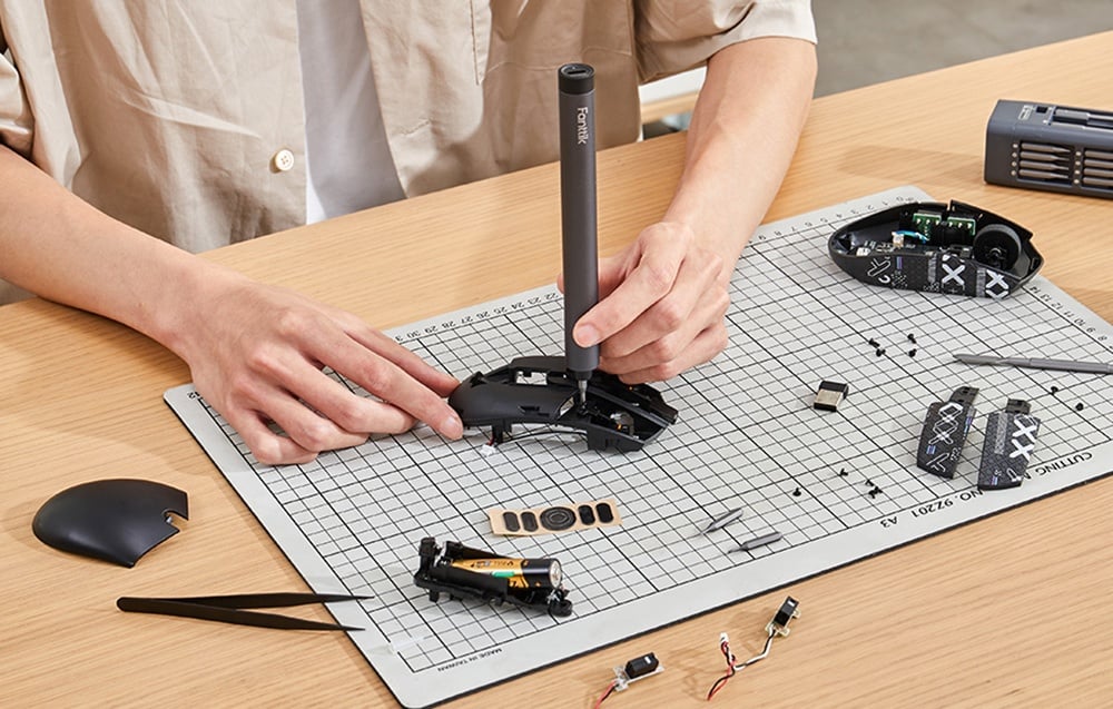 Un homme assis à son bureau répare une souris d'ordinateur avec un tournevis de précision.