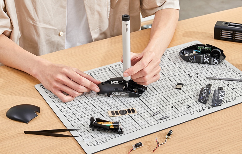 Un homme assis à son bureau répare une souris d'ordinateur avec un tournevis de précision.