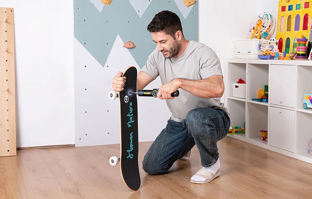 Un homme répare un skateboard dans la chambre d'un enfant avec une visseuse électrique.