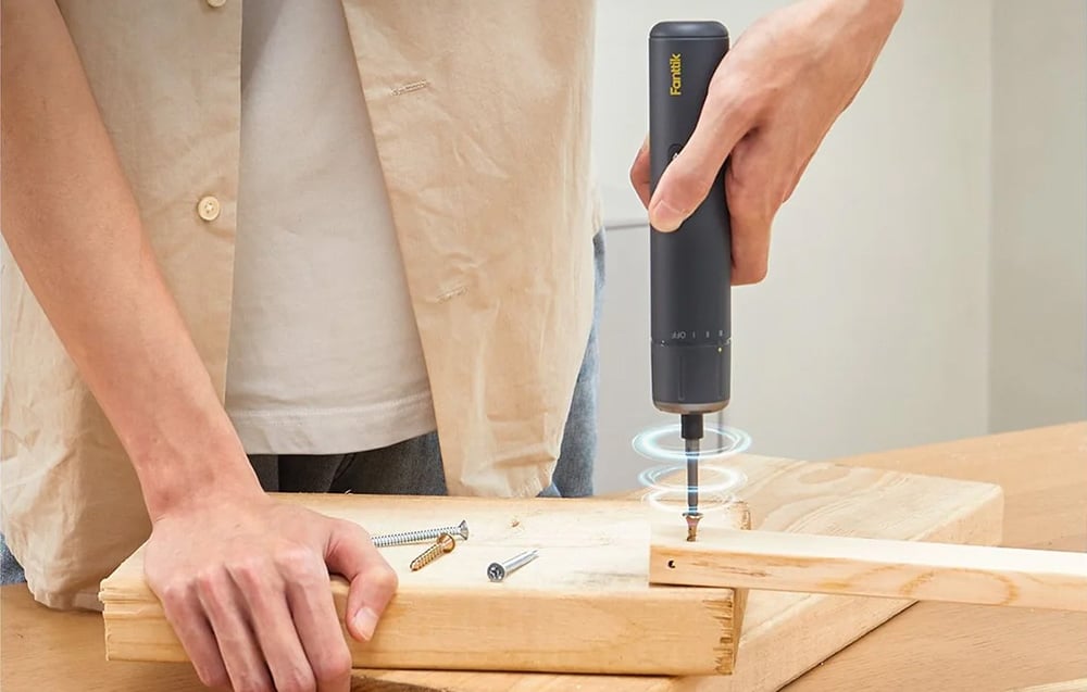 Un homme visse une bande en bois avec un tournevis électrique.