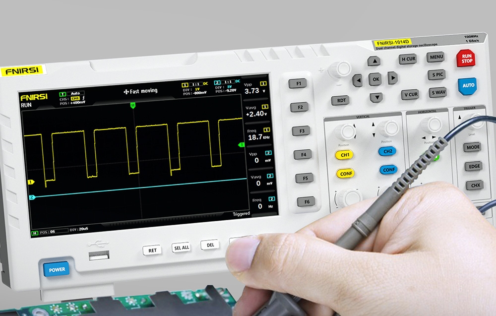 Ręka trzyma sondę podłączoną do oscyloskopu z kolorowym ekranem pokazującym żółty wykres prostokątny.