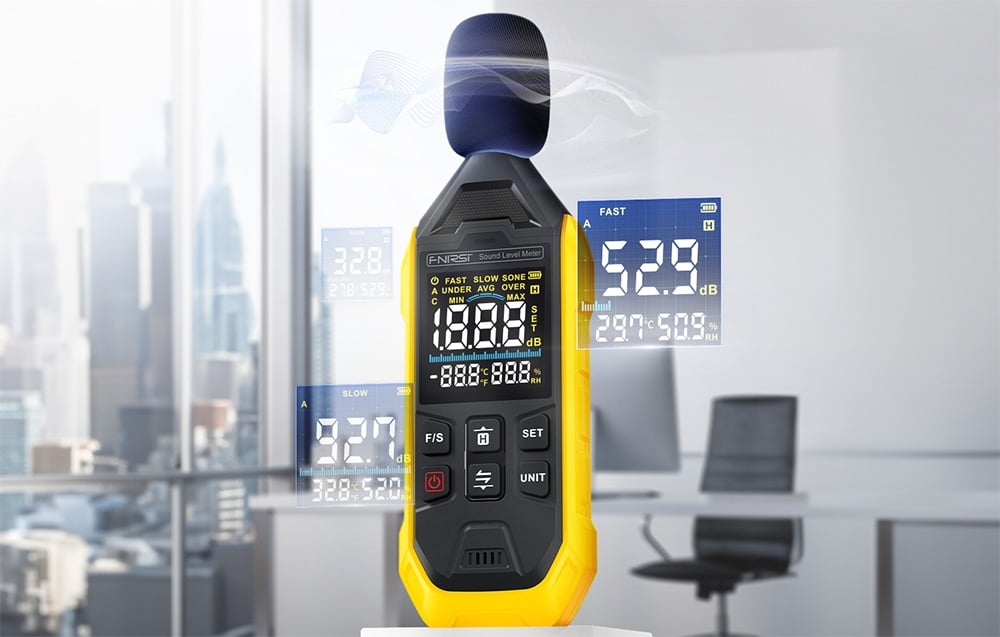 Mètre décibel avec protection de microphone et affichage montrant une mesure dans un bureau avec vue sur la ville.