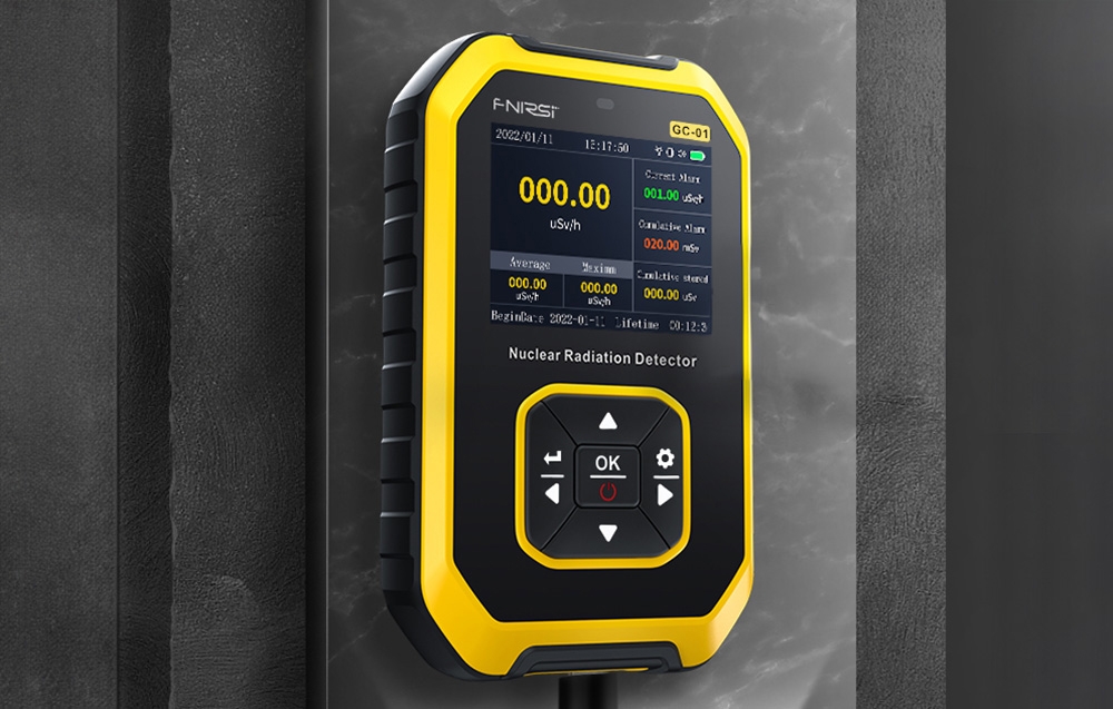Détecteur de radiation nucléaire dans un boîtier jaune et noir suspendu au mur, montrant l'écran avec les valeurs de mesure.