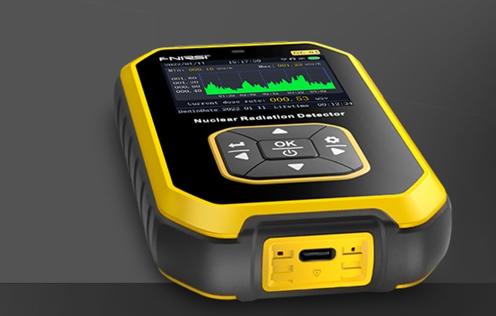 Détecteur de radiation nucléaire posé sur une surface grise avec un graphique de mesure visible à l'écran et un port USB-C sur le bord inférieur.