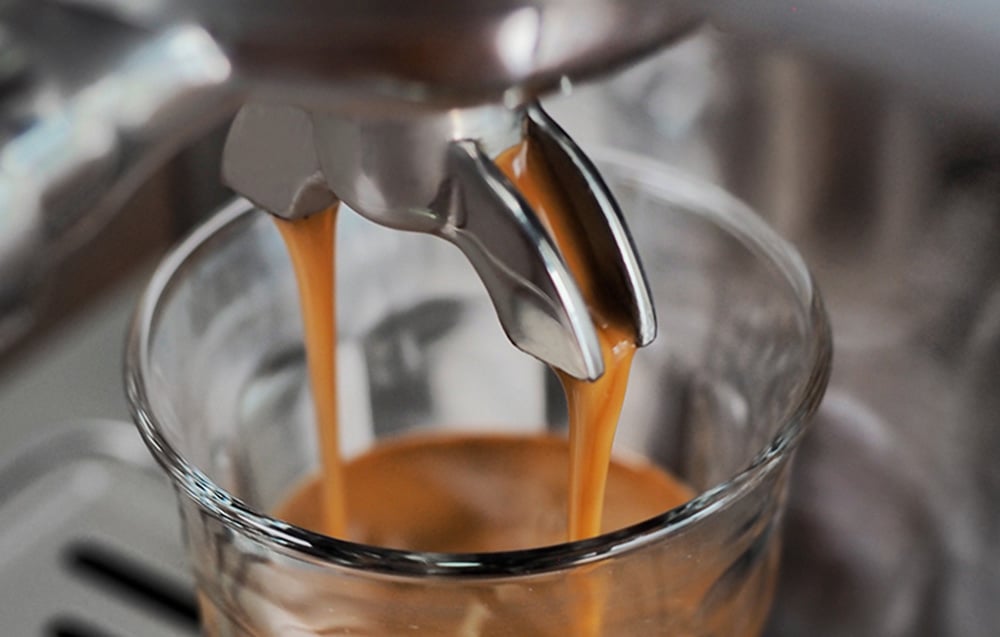 Gros plan du bec verseur de la machine à espresso, d'où s'écoule un flot de café chaud avec une mousse épaisse (crema) dans un verre.
