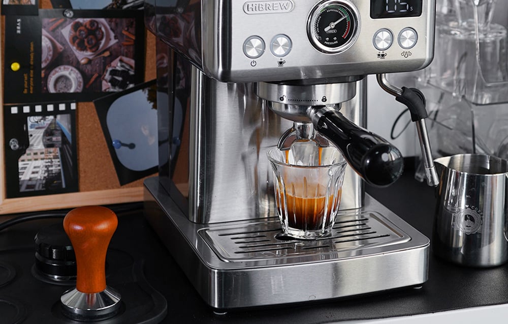 Machine à espresso HiBREW dans une cuisine, à côté d'accessoires de barista tels qu'un tamper en bois et un pichet à lait en métal.