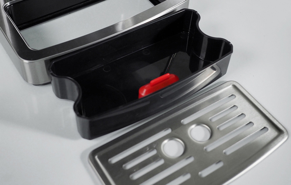 Le bac d'égouttage de la machine à espresso, démonté, montrant un conteneur d'eau en plastique, un flotteur rouge indiquant le niveau de remplissage, et une grille en métal.