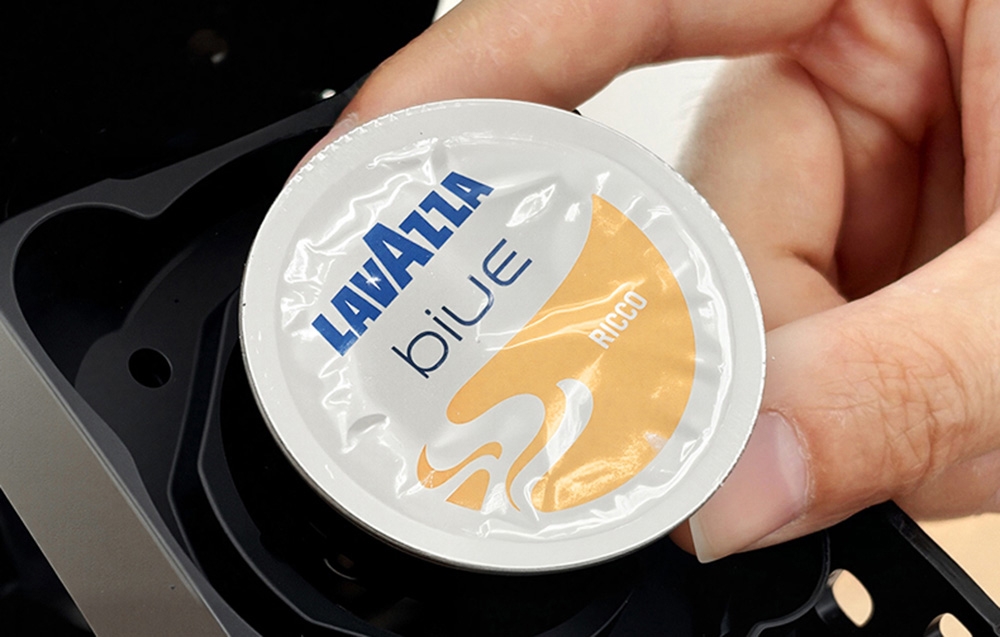 Main tenant une capsule Lavazza Blue Ricco au-dessus d'une machine à café ouverte