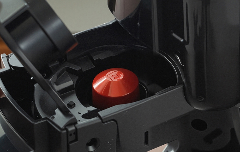 Chambre ouverte de la machine avec une capsule rouge placée dans le mécanisme