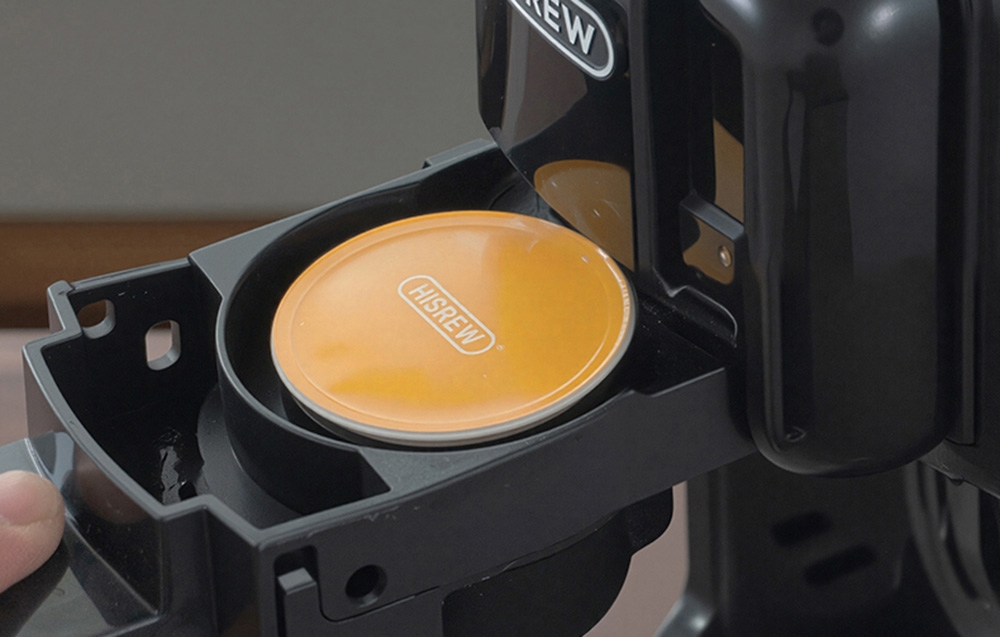 Capsule dorée HiBREW placée dans la chambre ouverte de la machine à café