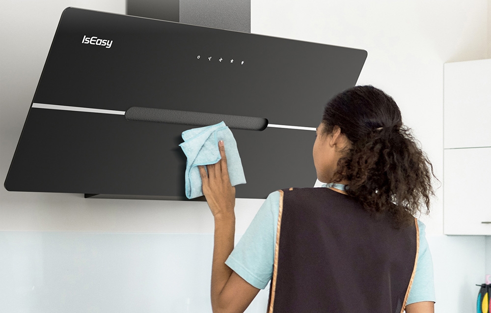 Une femme nettoie une hotte noire avec un chiffon bleu dans une cuisine lumineuse