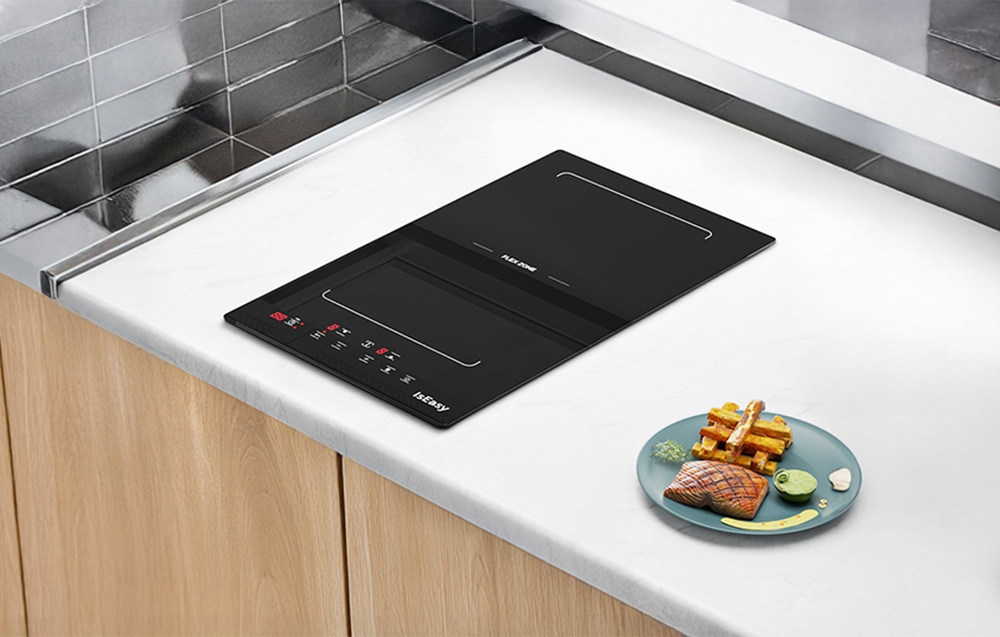 Plaque à induction noire intégrée dans un plan de travail de cuisine blanc à côté d'une assiette de saumon grillé et de frites