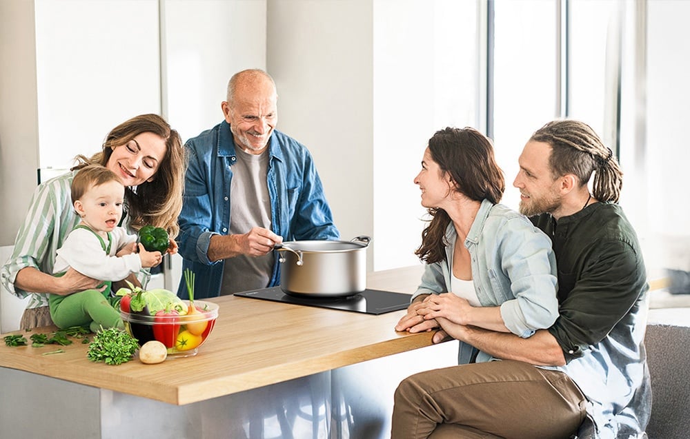 Une famille de cinq personnes cuisinant ensemble dans une cuisine moderne au plan de travail avec des légumes et une casserole