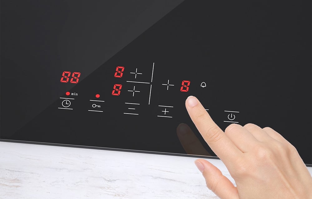 Une main touche le panneau de contrôle de la plaque à induction avec des chiffres rouges et des symboles blancs