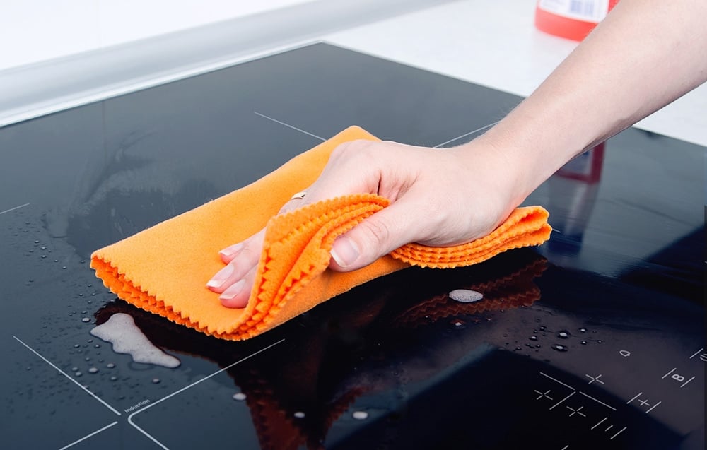 Une main avec un chiffon en microfibre orange nettoie une plaque à induction noire