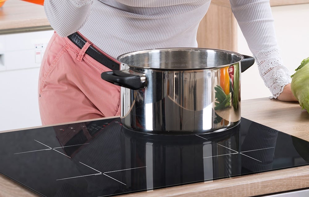 Une femme en pantalon rose cuisine dans une grande casserole en acier inoxydable sur une plaque à induction