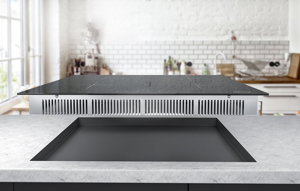 Plaque à induction avec système de ventilation visible au-dessus du plan de travail encastré dans une cuisine lumineuse