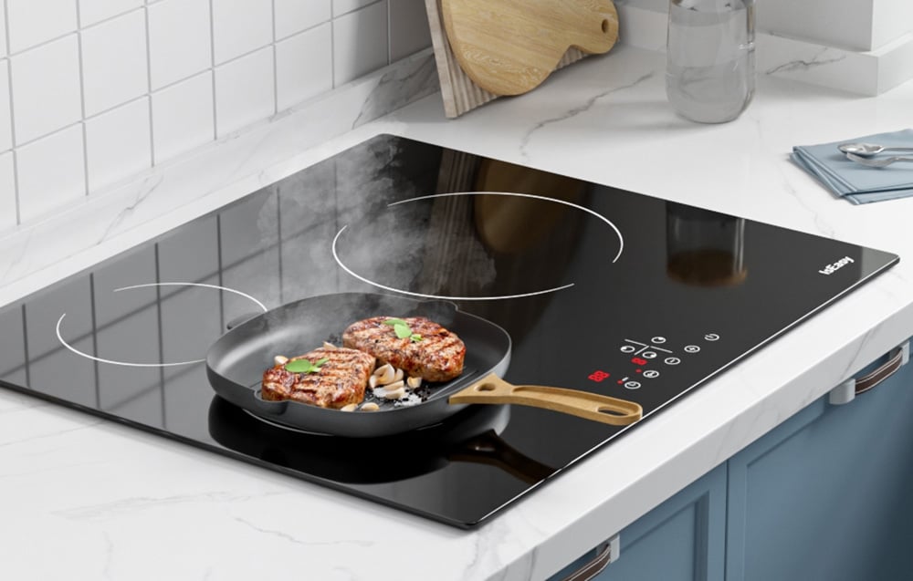 Plaque à induction avec poêle noire et côtelettes grillées dans une cuisine lumineuse avec carrelage blanc