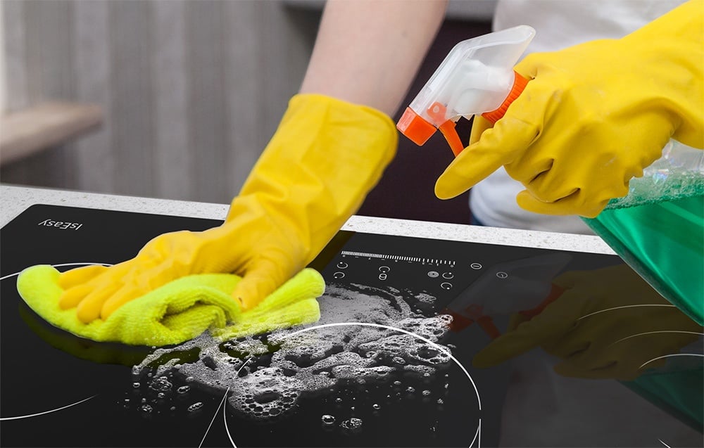 Mains en gants jaunes nettoient la plaque à induction avec un produit chimique et un chiffon jaune