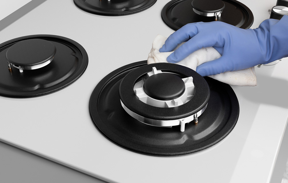 Une main gantée de bleu nettoie le brûleur de la cuisinière à gaz avec un chiffon
