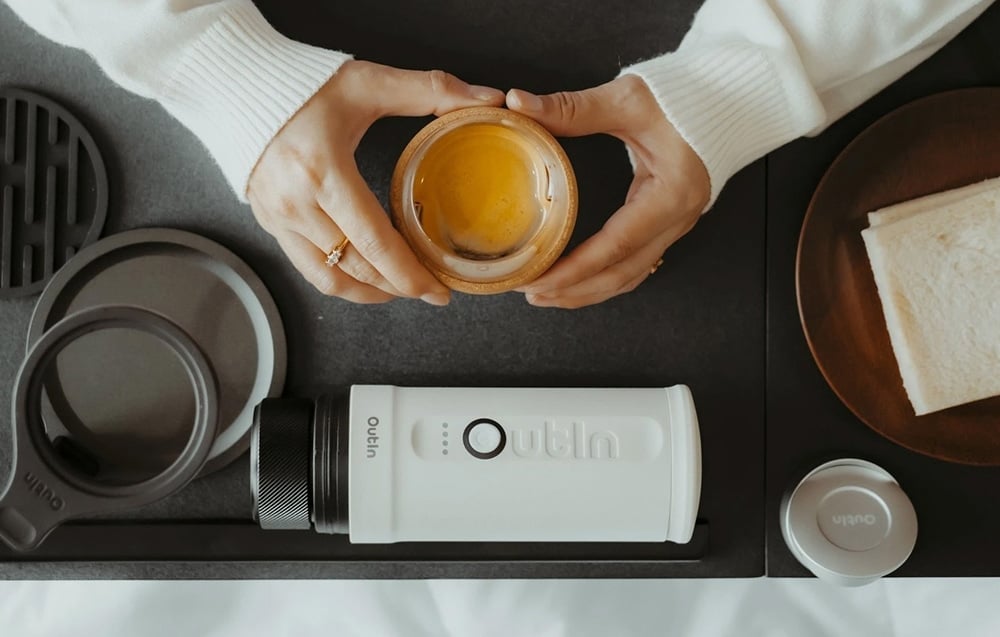 Une femme tient une tasse de café. À côté d'elle, sur la table, se trouve la machine à café Outin.