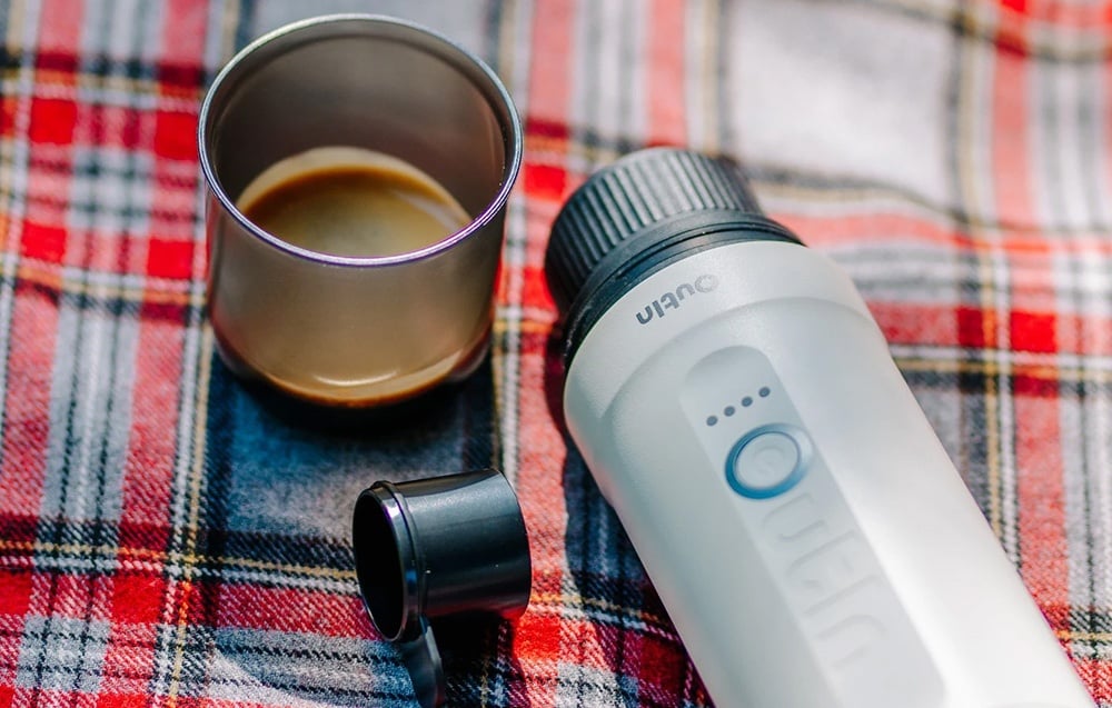 La machine à café sans fil Outin, une tasse et un verre doseur reposent sur une nappe à carreaux rouges.