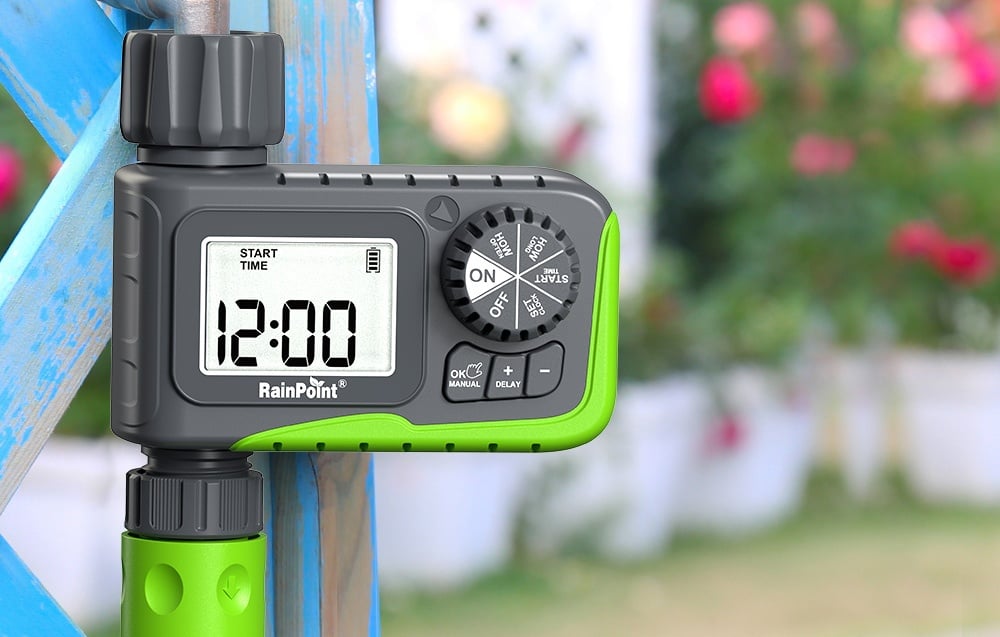 Minuteur d'arrosage fixé à une structure métallique bleue avec des fleurs en arrière-plan