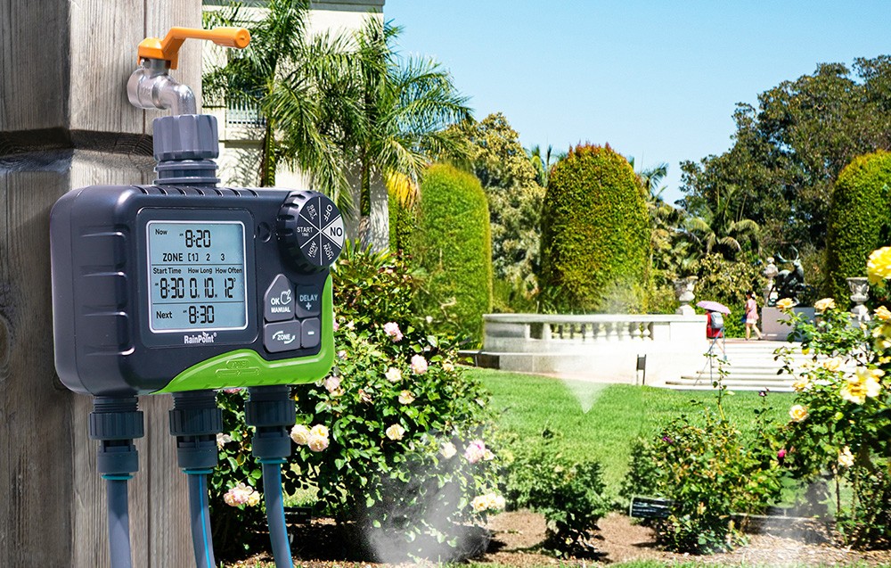 Contrôleur d'arrosage RainPoint fixé à un poteau en bois dans le jardin, arroseurs allumés.