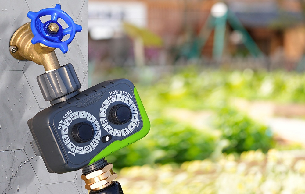 Programmateur d'arrosage connecté à un robinet de jardin avec un robinet bleu, en arrière-plan des potagers