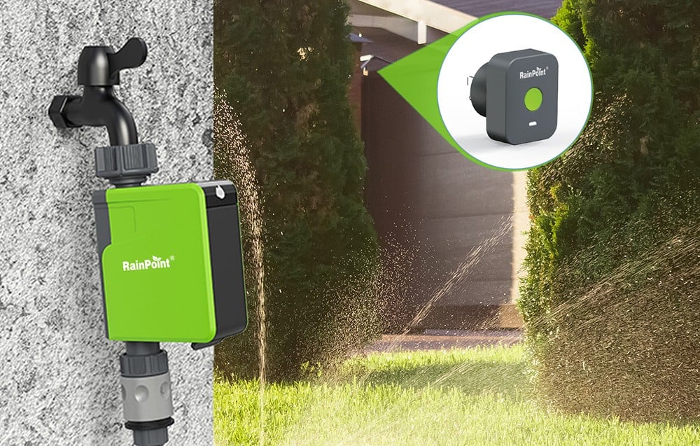 Contrôleur d'irrigation RainPoint monté sur un mur gris, avec un jardin irrigué en arrière-plan.