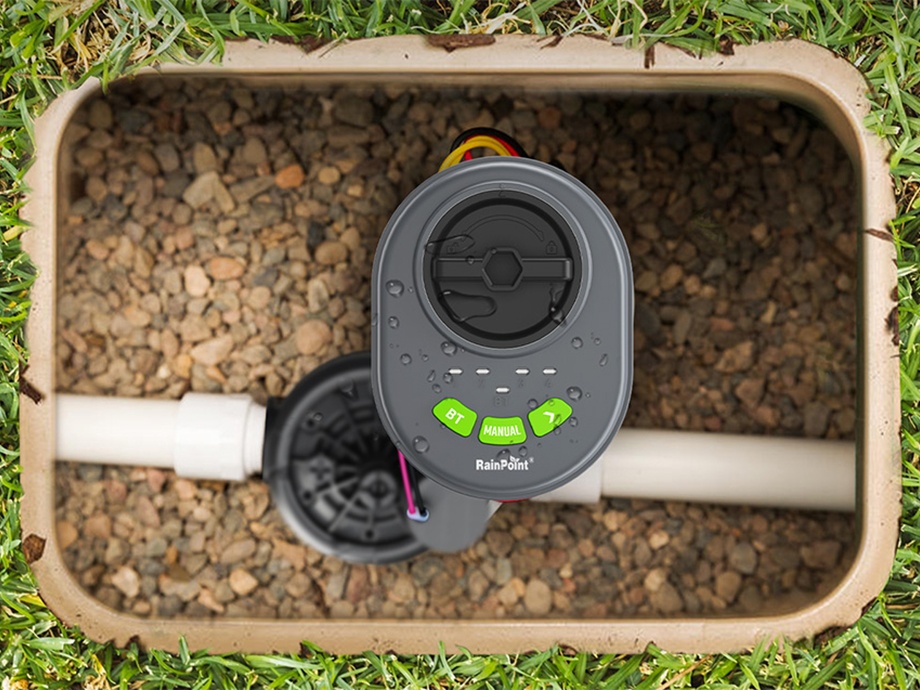 Contrôleur RainPoint dans une petite boîte de vannes remplie de gravier, vue de dessus.