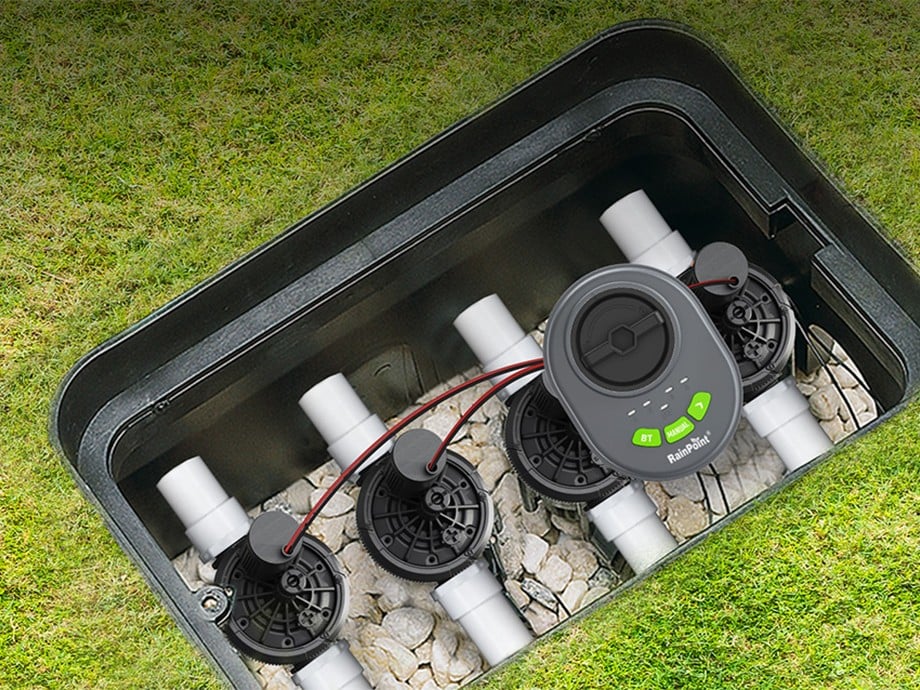 Contrôleur RainPoint installé dans une boîte avec quatre vannes sur fond de pelouse.