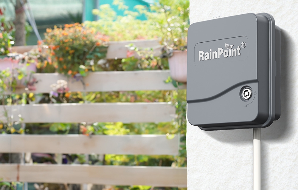 Contrôleur RainPoint fermé monté au mur avec vue sur le jardin en arrière-plan.