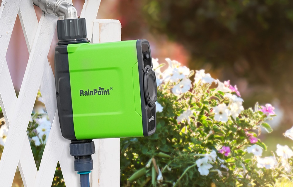 Contrôleur RainPoint installé sur une clôture blanche avec des fleurs en arrière-plan