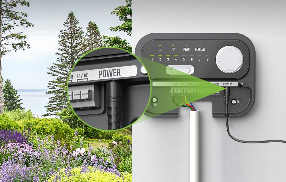 Un contrôleur d'arrosage RainPoint connecté à l'alimentation, avec des fleurs colorées en arrière-plan.